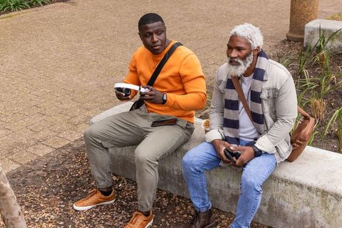 African american friends trying vr headset while sitting on urban plaza bench