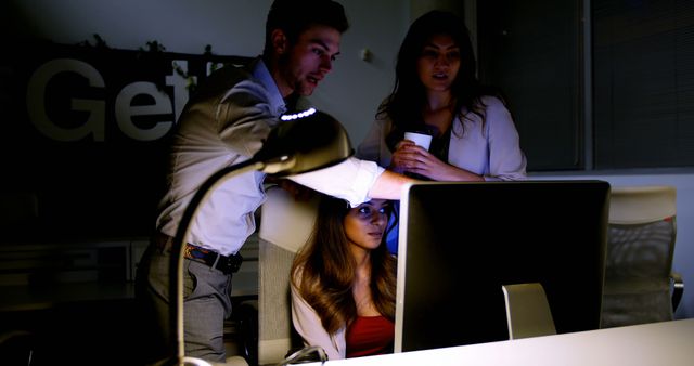 Business team collaborating late at night in modern office, focused on project displayed on computer screen. Useful for illustrating concepts of teamwork, dedication, long hours, professional collaboration, or late-night work culture.