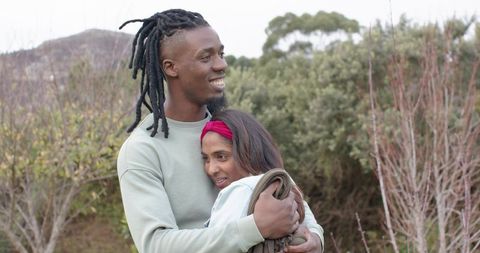 Interracial couple embracing in meadow outdoors, African American man holding Indian woman