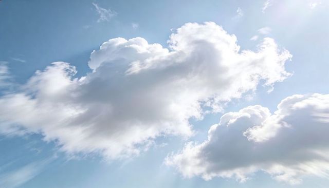 Sunlit cumulus clouds drifting across clear blue sky with soft sun rays and wispy edges