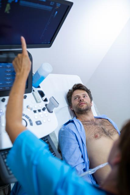 Man lying on examination table receiving abdominal ultrasound from healthcare professional in hospital. Useful for medical, healthcare, diagnostic, and treatment-related content.
