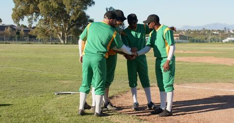 Cricket team huddling on pitch before match, green uniforms, community league teamwork