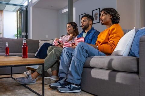 Friends watching movie on sofa sharing popcorn and bottled drinks in modern living room