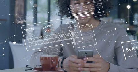 Man Holding Smartphone and Interacting with Augmented Data Overlay in Cafe Workspace
