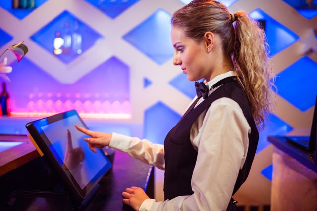 Side view of young barmaid using modern cash register at bar counter
