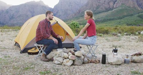 Couple sitting and chatting camping at mountain foothills by yellow dome tent and rock fire pit