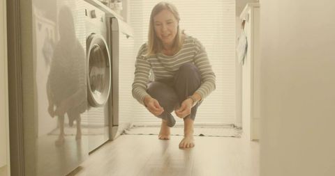 Woman in Modern Laundry Room Picking Up Item by Washing Machine