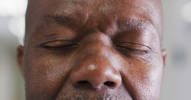 Close-up portrait of an elderly African American man with eyes closed, emphasizing wrinkles and skin texture. Useful for topics related to aging, mindfulness, meditation, serenity, and inner peace. Suitable for healthcare, wellness, and senior lifestyle projects.