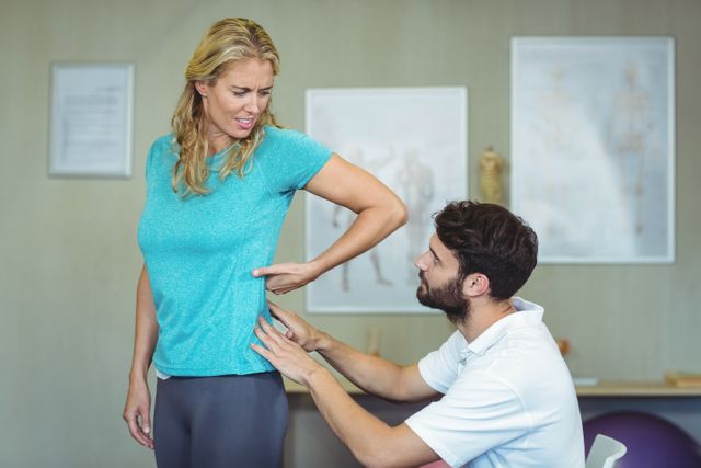 Physiotherapist examining woman's back pain in clinic. Ideal for use in healthcare, medical, and wellness contexts. Can be used in articles, blogs, and advertisements related to physical therapy, pain management, and rehabilitation services.