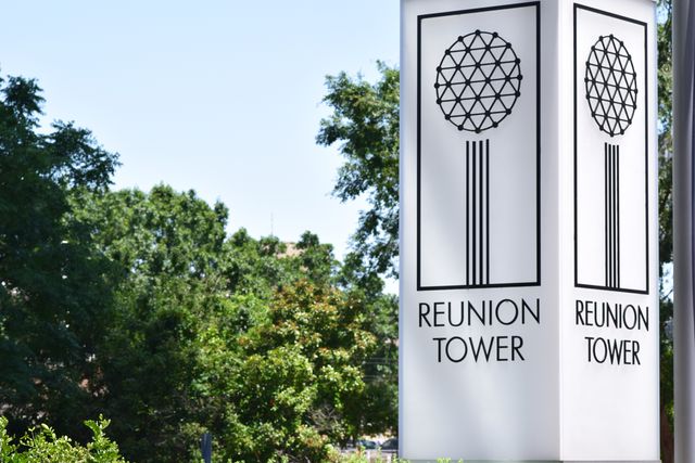 A close-up of the Reunion Tower signage set against lush green foliage. Ideal for travel magazines, tourism websites, or marketing materials promoting Dallas landmarks and attractions.