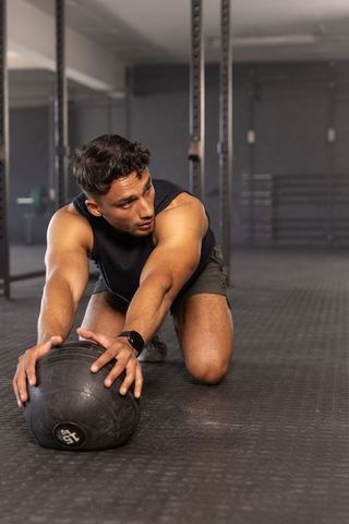 Athletic man kneeling pushing 15 lb medicine ball in functional strength workout in gym