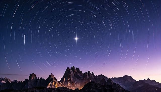 Jagged alpine peaks glowing under circular star trails around bright guiding star at twilight