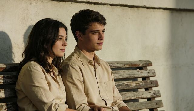 Young couple sitting on weathered wooden bench in sunlit yard, contemplative and quietly calm