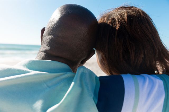 This image shows a senior couple embracing while looking at the ocean on a sunny day. It is perfect for use in advertisements or articles related to retirement, love, lifestyle, and holiday enjoyment. It can also be used in brochures or websites promoting travel, leisure activities, and senior living.