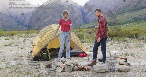 Couple building campfire in mountain valley near yellow dome tent for outdoor adventure
