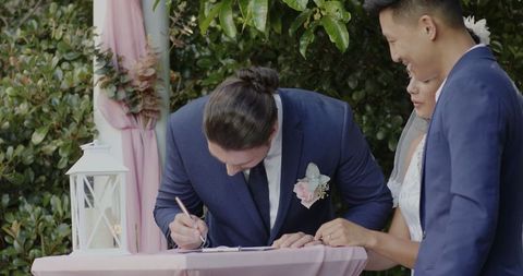 Bride signing wedding documents outdoors with groom and witness