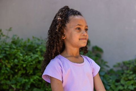 African american girl looking confident in lavender shirt outdoors with garden greenery