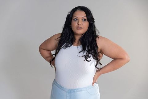 Confident curvy woman posing hands on hips wearing white ribbed top and light denim