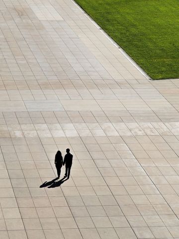 Couple walking on vast paved area near lush green grass