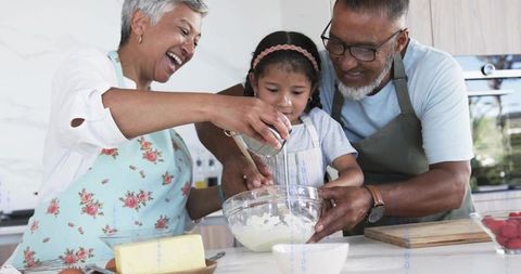 Grandparents and Granddaughter Baking Together in Bright Kitchen Mixing Batter