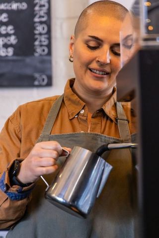 Barista steaming milk for latte art behind counter in modern minimalist coffee shop