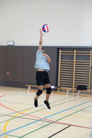 African american teen jumping to spike volleyball in school gymnasium