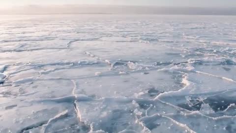 Panning over fractured pack ice on frozen sea revealing distant horizon and open cracks