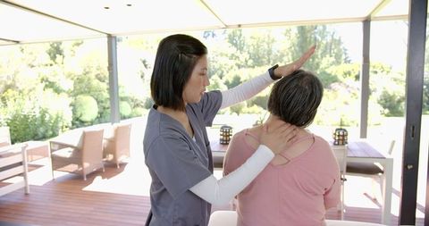 Female physiotherapist assisting senior woman with neck exercises