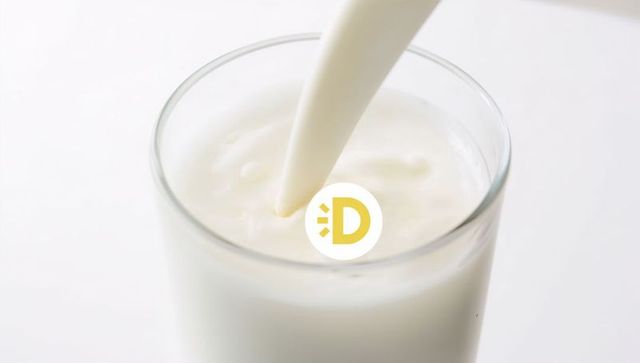 Pouring milk forming gentle swirl in clear glass tumbler with yellow logo sticker