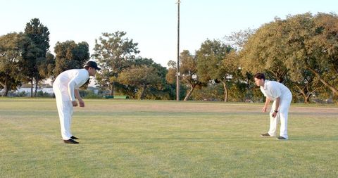 Two cricketers standing in fielding stance on green outfield during warm light practice