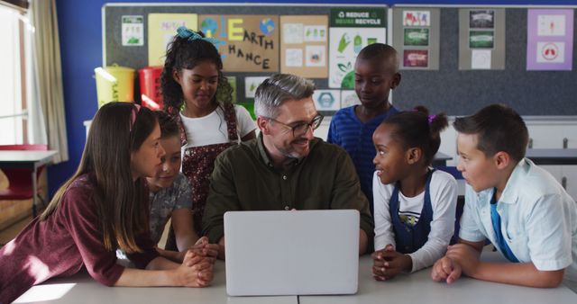 Diverse male teacher and group of schoolchildren looking at laptop. children at primary school in summer.