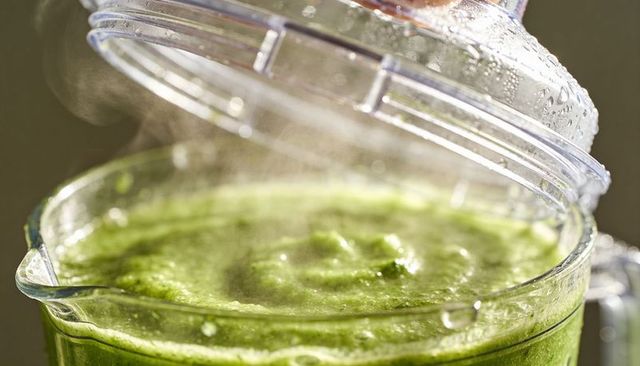 Steaming frothy green smoothie blending in clear plastic blender pitcher with condensation
