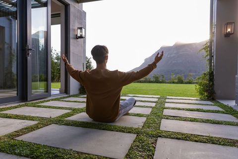 Man meditating on modern patio with stone pavers and mountain view at sunrise