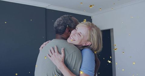 Hugging mature couple celebrating new home with gold confetti in minimalist interior
