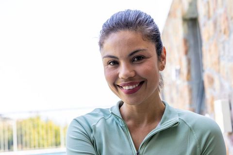 Smiling woman on balcony in light green zip-up activewear enjoying sunny terrace lifestyle