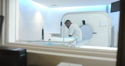 African american man sitting on ct scanner bed covering face in hospital gown