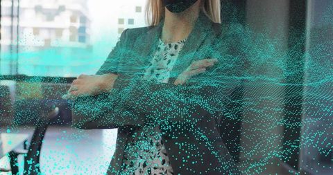 Professional woman standing with crossed arms wearing mask and teal data overlay