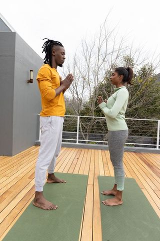 Couple practicing partner yoga on rooftop deck facing each other in namaste pose