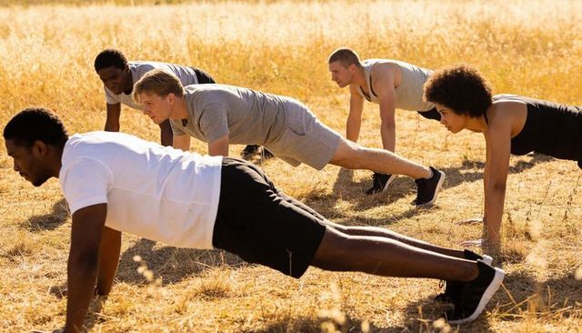 Outdoor group holding plank for core strength and team fitness in sunlit meadow
