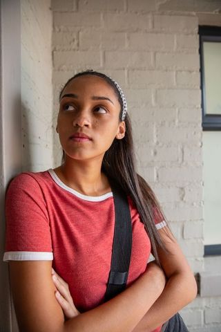 Teenager leaning against white brick hallway wall wearing headband and bag strap