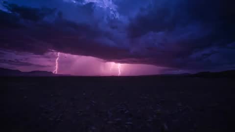 Flashing lightning storm illuminating desert plain with purple sky and shelf cloud