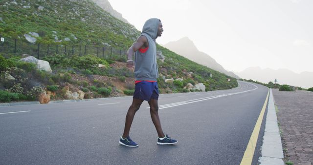 African american man wearing a hoodie performing stretching exercise and running on the road. fitness and healthy lifestyle concept