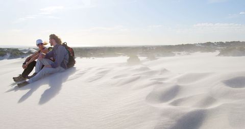 Couple relaxing on sunlit desert dunes embracing serene landscape