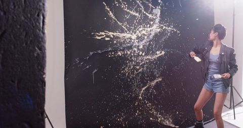 Female artist throwing paint on black studio backdrop creating dramatic splatter art motion