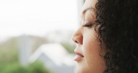 Serene mid-adult woman resting with eyes closed at window, profile closeup, soft bokeh