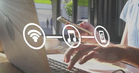 Multitasking remote worker typing laptop while holding smartphone sunlit cafe wi-fi icons