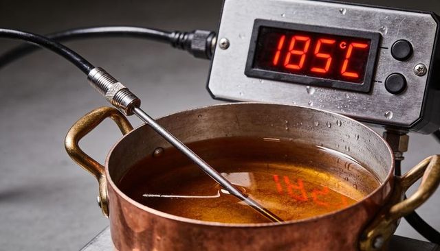 Copper pot with thermocouple probe measuring 185°c over amber liquid for culinary and lab use