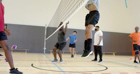 Multiracial men jumping at net during indoor volleyball match showing high-energy teamwork