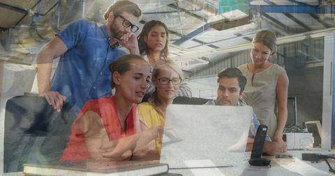 Diverse creative team collaborating around laptop in modern open industrial office