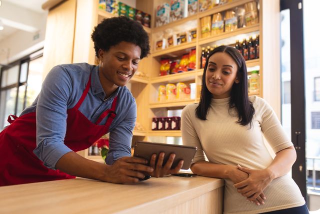 Smiling african american and biracial young owners using digital tablet at counter in cafe. unaltered, cafeteria, barista, occupation, food, wireless technology, coworker and small business concept.